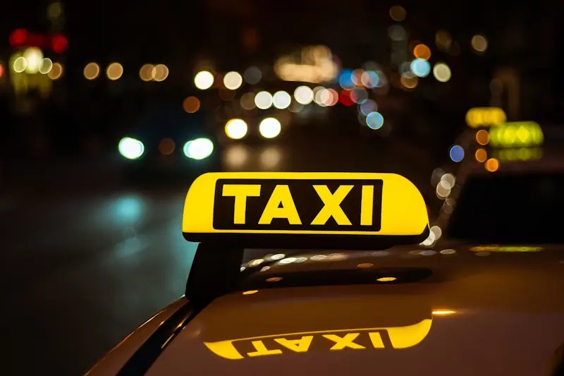 Startseite 12 Leuchtendes gelbes TAXI-Schild auf dem Dach eines Fahrzeugs vor unscharfem nächtlichem Stadtverkehr mit Lichtern im Berliner Nachtleben.